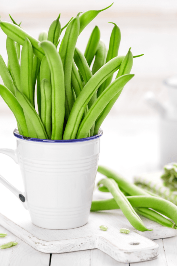 green beans standing up in a white cup on a white cutting board